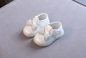 Nahaufnahme weißer Baby-Prinzessin-Schuhe mit funkelnden Perlen- und Strassschleifen.