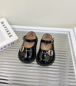 Vista detallada de zapatos Mary Jane de charol negro para bebé con hebillas doradas.
