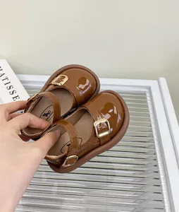 Detalle de zapatos Mary Jane de charol marrón para bebé niña con hebilla dorada.