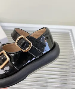 Primer plano de zapato de charol negro para bebé con hebilla dorada y cierre velcro
