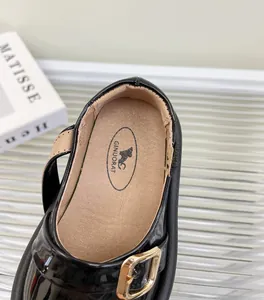 Primer plano de zapatos Mary Jane para bebé en charol negro con hebilla dorada y suela blanda