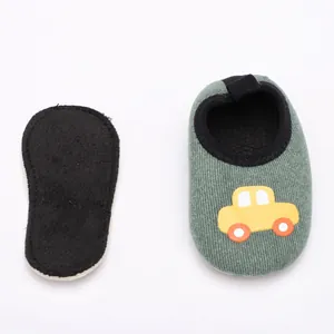 Gros plan de chaussons bébé en velours vert avec motif voiture jaune et semelle antidérapante