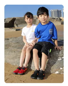 Asian children wearing red and black non-slip water shoes sitting on a rock at the beach