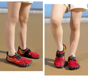Close-up of kids red water shoes with black dot pattern worn on a sandy beach under sunlight