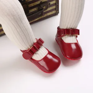 Close-up of red patent leather baby Mary Jane shoes with bow and soft sole.
