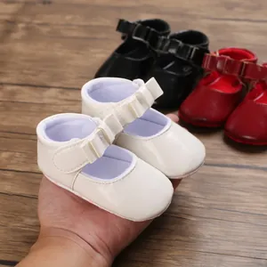 Close-up view of white infant girl princess walking shoes with charming bow detail held in hand
