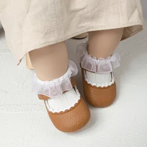 Close-up van bruine kunstlederen baby prinsessenschoenen met delicate witte kanten ruches.
