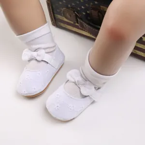 Primer plano de zapatos de princesa para bebé blancos con bordado floral y un lazo