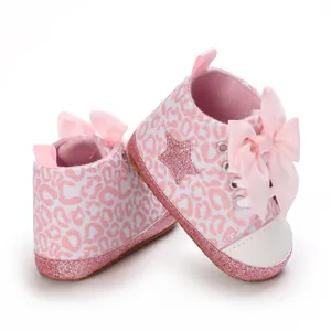 Detalle de zapatos de bebé con estampado de leopardo rosa, lazos y suelas de purpurina