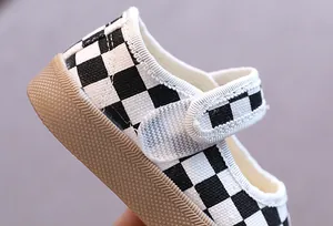 Détail d'une chaussure pour bébé avec motif en damier noir et blanc et semelle souple.