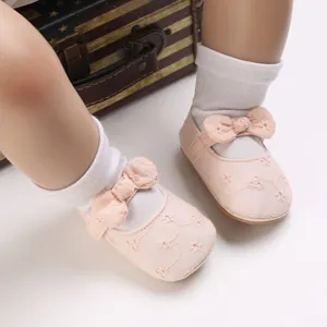 Detalle de zapatos rosa de princesa para bebé con bordado y un lazo decorativo.