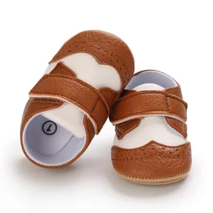Close-up of brown and white baby walking shoes with brogue details and Velcro straps.
