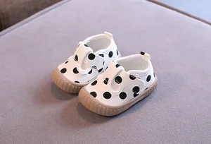 Detailed view of white canvas baby walking shoes with black polka dots and soft rubber soles
