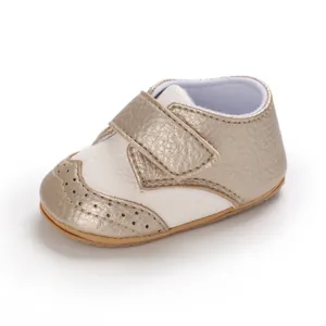 Close-up detail of golden and white metallic baby brogue walking shoes with velcro strap