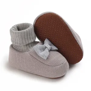 Détail de chaussons bébé tricotés gris avec semelles antidérapantes et nœud décoratif.