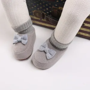 Détail de chaussures bébé en tricot gris avec un joli nœud et revers côtelé doux.