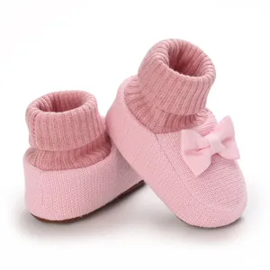Gros plan de chaussons en tricot rose pour bébé avec nœud et revers côtelés doux.