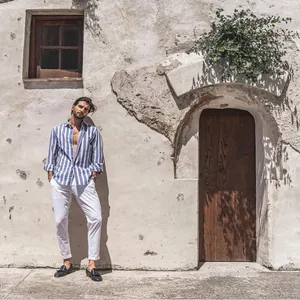 Casual men's blue and white striped long sleeve shirt styled with white trousers outdoors