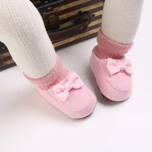 Gros plan de chaussons pour bébé tricotés roses avec une semelle souple et un nœud.
