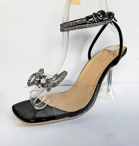 Close-up of elegant black high-heeled sandals with a rhinestone bow and clear PVC strap.