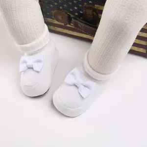Vue détaillée de chaussons en tricot blanc pour bébé avec un joli nœud et semelle souple