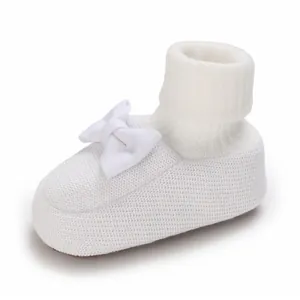 Détail d'un chausson bébé blanc en maille souple orné d'un joli petit nœud décoratif