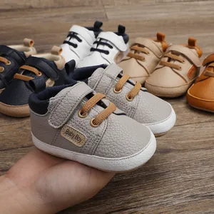 Close-up of gray faux leather baby walking shoes with "Baby Boy" label held in hand.