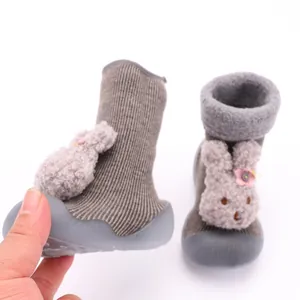 Detalle de zapatos calcetín de punto para bebé con conejo de peluche y suela de goma flexible.
