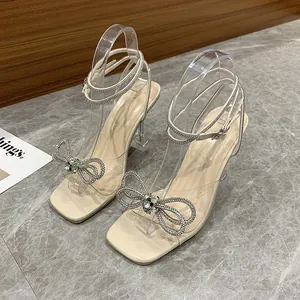 Elegant cream sandals featuring rhinestone bow detail and transparent straps macro shot