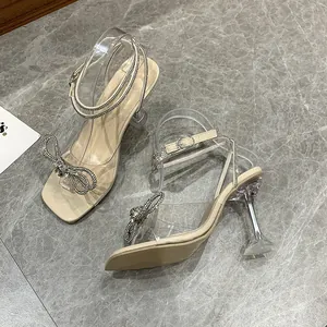 Elegant cream sandals with a rhinestone bow and transparent heels on marble floor