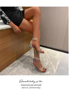 Detail of iridescent high-heeled sandals with rhinestone bow worn by a model