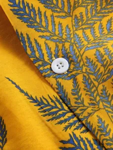 Macro detail of men's summer beach shirt with blue fern print on yellow fabric