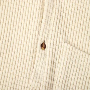 Detail shot of the waffle knit fabric texture and button on a beige men's shirt