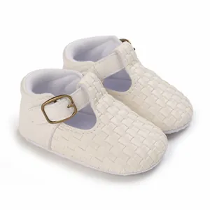 Nahaufnahme von cremefarbenen Babyschuhen mit Webstruktur und metallischem Schnallenverschluss.