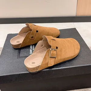 Side view of brown suede clogs with adjustable buckle on a textured surface