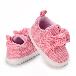 Close-up of pink knitted baby shoes with a large decorative bow and white sole.
