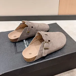 Close-up detail of stylish grey suede mules featuring a rustic buckle strap and cork sole