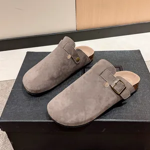 Detail view of grey suede closed-toe cork mules with buckle strap on a black box.