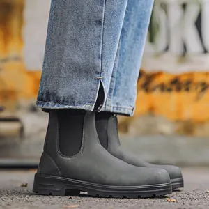 Détail rapproché de bottines Chelsea en cuir mat gris foncé portées avec un jean bleu.