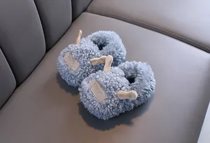 Close-up of blue fluffy children's winter slippers with cute 3D horn detail on gray sofa