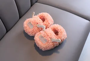 Detailopname van roze pluizige kindersloffen met schattige oortjes op een grijze bank.