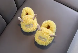 Schattige gele pluche kindersloffen met kleine hoorns op een zachte grijze ondergrond