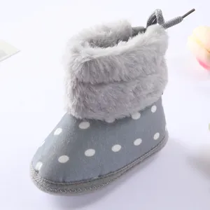 Detalle de botas de bebé con lunares grises, ribete de piel sintética y suela suave.