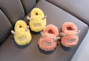 Close-up of yellow and pink fuzzy sheep-style children's slippers on a grey sofa