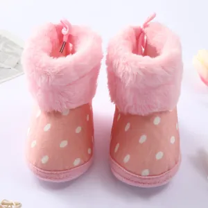 Detalle de botas de piel rosa con lunares para bebé con cuello de felpa suave para invierno.