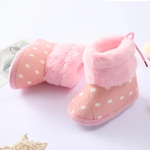 Primer plano detallado de botines rosas para bebé con lunares y ribete de pelo suave