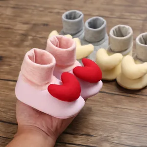 Nahaufnahme von rosa Baby-Laufsocken mit rotem Herz-Detail, in der Hand gehalten