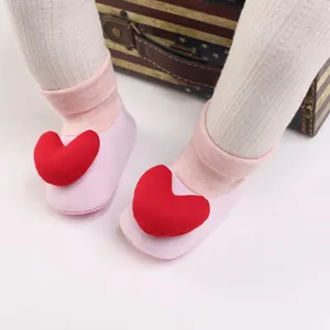 Nahaufnahme von rosa Baby-Laufsocken mit großen roten Plüschherz-Verzierungen