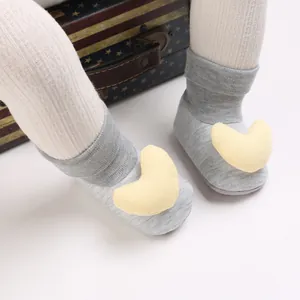 Nahaufnahme grauer Strick-Babysocken mit gelber Herzdeko an kleinen Babyfüßen