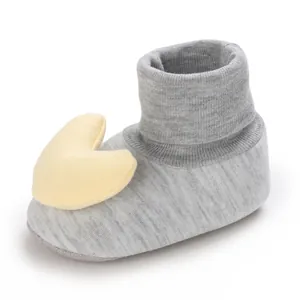 Detailansicht einer grauen Strick-Babysocke mit einer gelben Plüsch-Herzverzierung